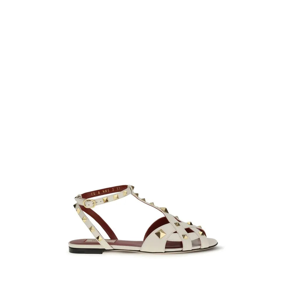 Valentino Garavani beige goatskin flat sandals with antique brass studs, caged toe, and ankle buckle strap.