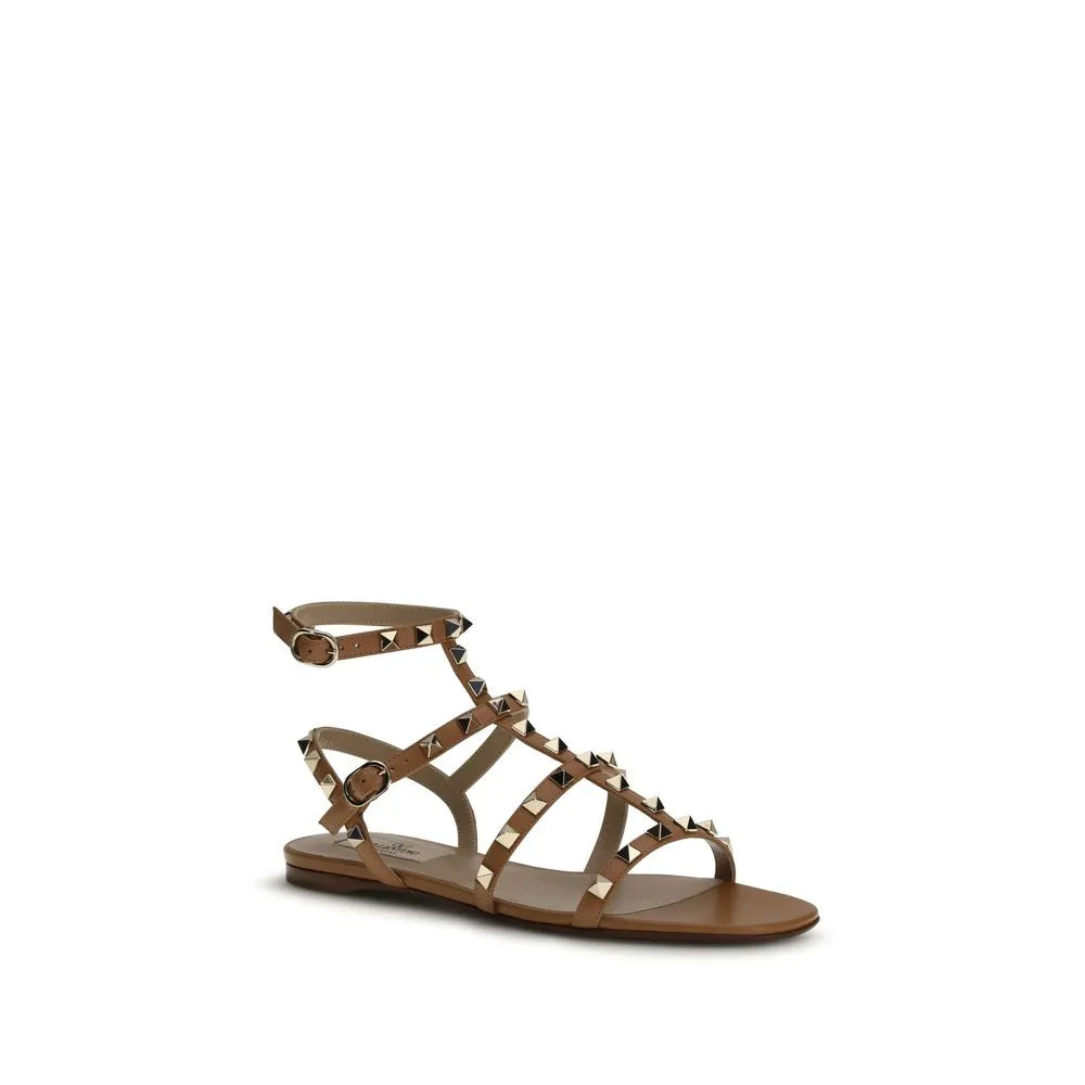 Valentino Garavani Rockstud beige calf leather flat sandals with gold pyramid studs, round toe, and adjustable ankle strap.