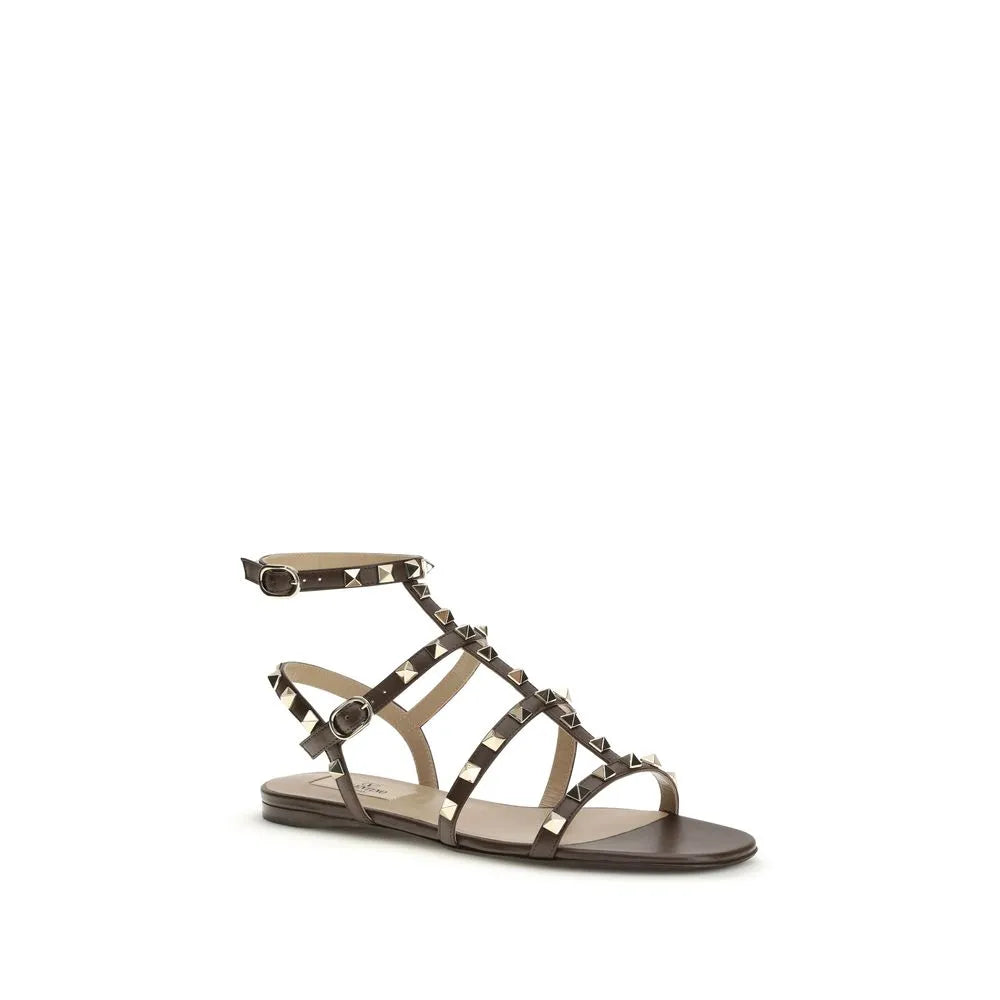 Dark brown calf leather flat gladiator sandals with gold pyramid studs and adjustable ankle strap.