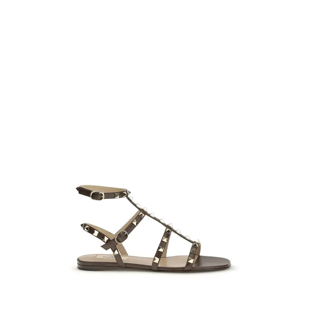 Brown calf leather Valentino Garavani Rockstud flat sandals featuring gold pyramid studs, multiple straps, and an adjustable ankle buckle.